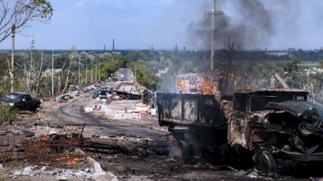 
 Sebuah truk terlihat hancur dan terbakar di jembatan yang menghubungkan Severodoonetsk dan Lysychansk, Luhansk, Ukraina Timur pada 28 Mei 2022. (FOTO: The Moscow Times/TASS via suara.com)